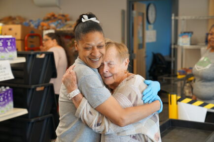 Two women hug inside a food pantry