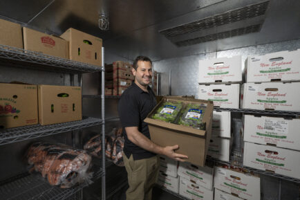 Man holding a box of produce in a walk-in freezer at a food pantry